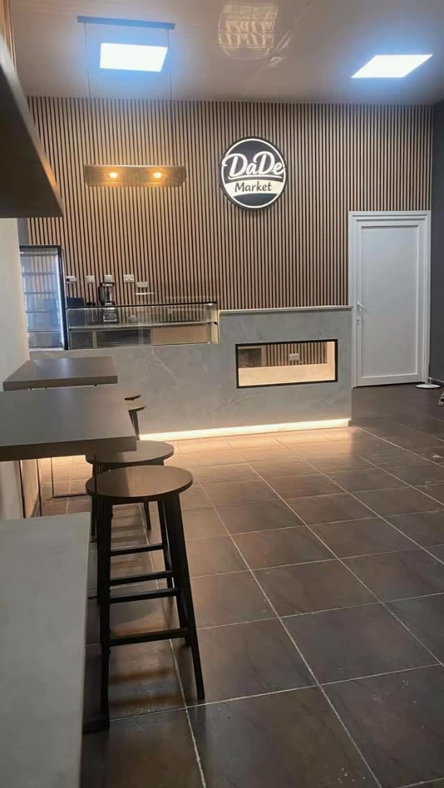 Interior of DaDe Market checkout area with wood slat wall, circular logo, and counter with bar stools.