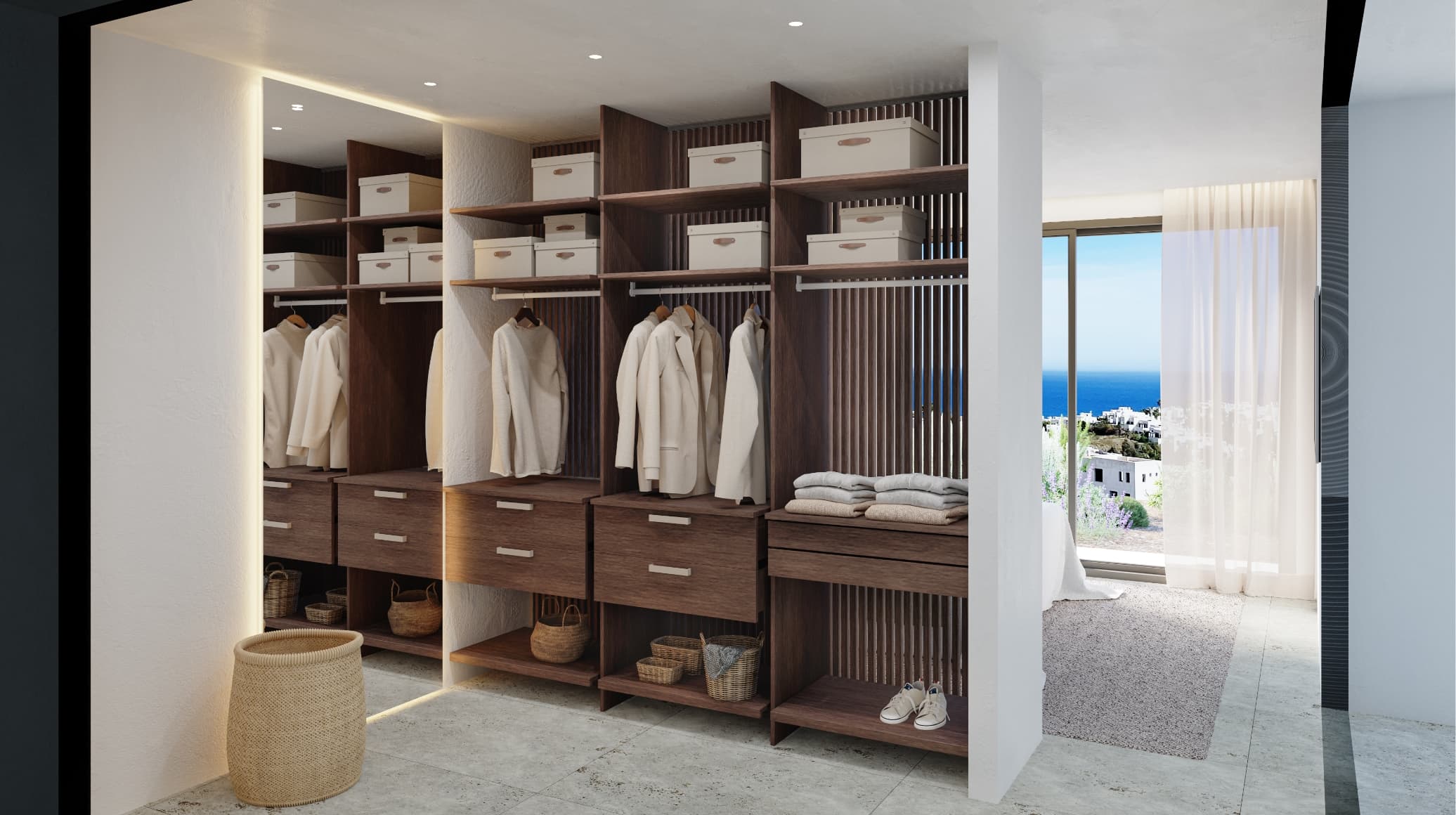 Contemporaneo_vestidor - MiraCasa Walk-in closet with dark wood shelves, beige coats on hangers, labeled storage boxes, and woven baskets below. Window view to the sea on the right.