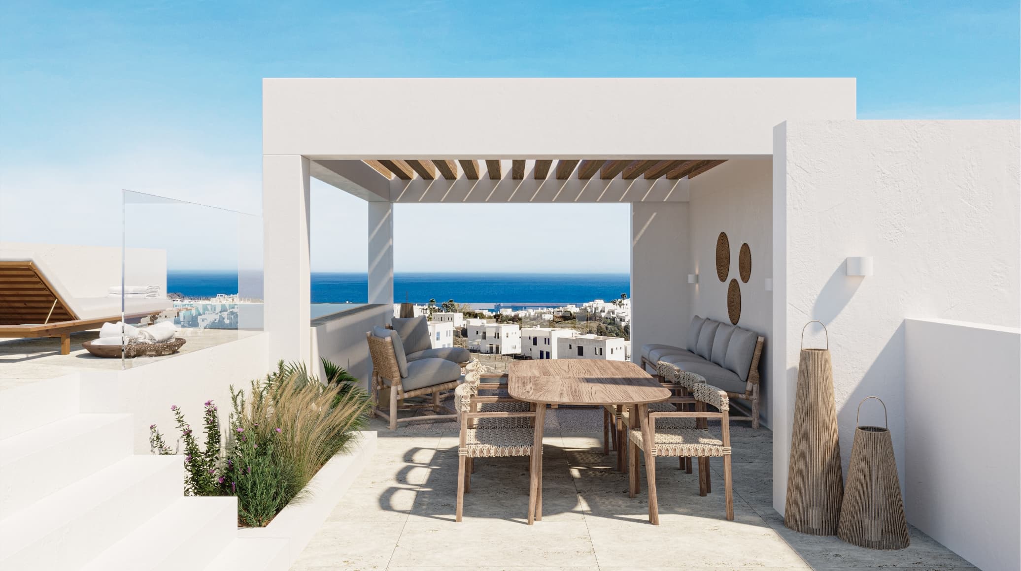 Mediterraneo_masterbed_003-1 - MiraCasa Open-air white patio with a wooden dining table and woven chairs, overlooking the blue sea and distant town.