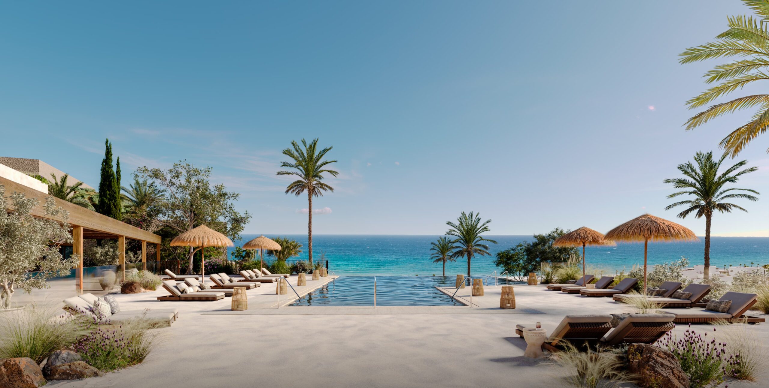 Resort poolside with loungers, thatched umbrellas, palm trees, and the ocean in the background under a clear blue sky.